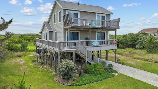 A two-story wooden house with a balcony and a deck, surrounded by greenery. - Head for the beach and settle into Migration! (South Nags Head)