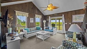 A cozy room with wooden walls, a ceiling fan, a sofa, a patterned armchair, and a coffee table. - Head for the beach and settle into Migration! (South Nags Head)