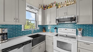 A modern kitchen with grey cabinets, a stainless steel dishwasher, a built-in oven, and a microwave. - Head for the beach and settle into Migration! (South Nags Head)