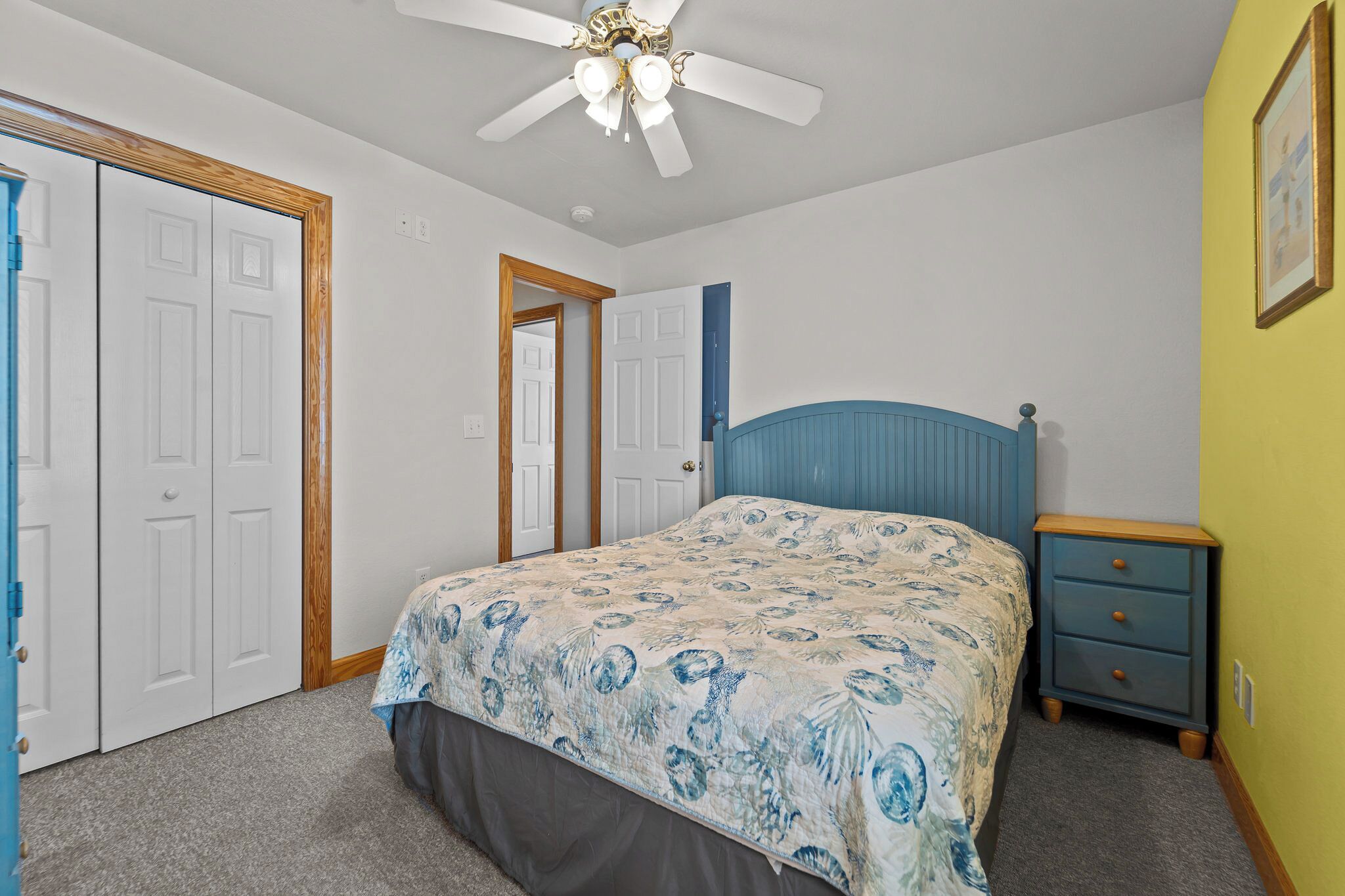 A bedroom with a bed, a nightstand, a ceiling fan, and a door.