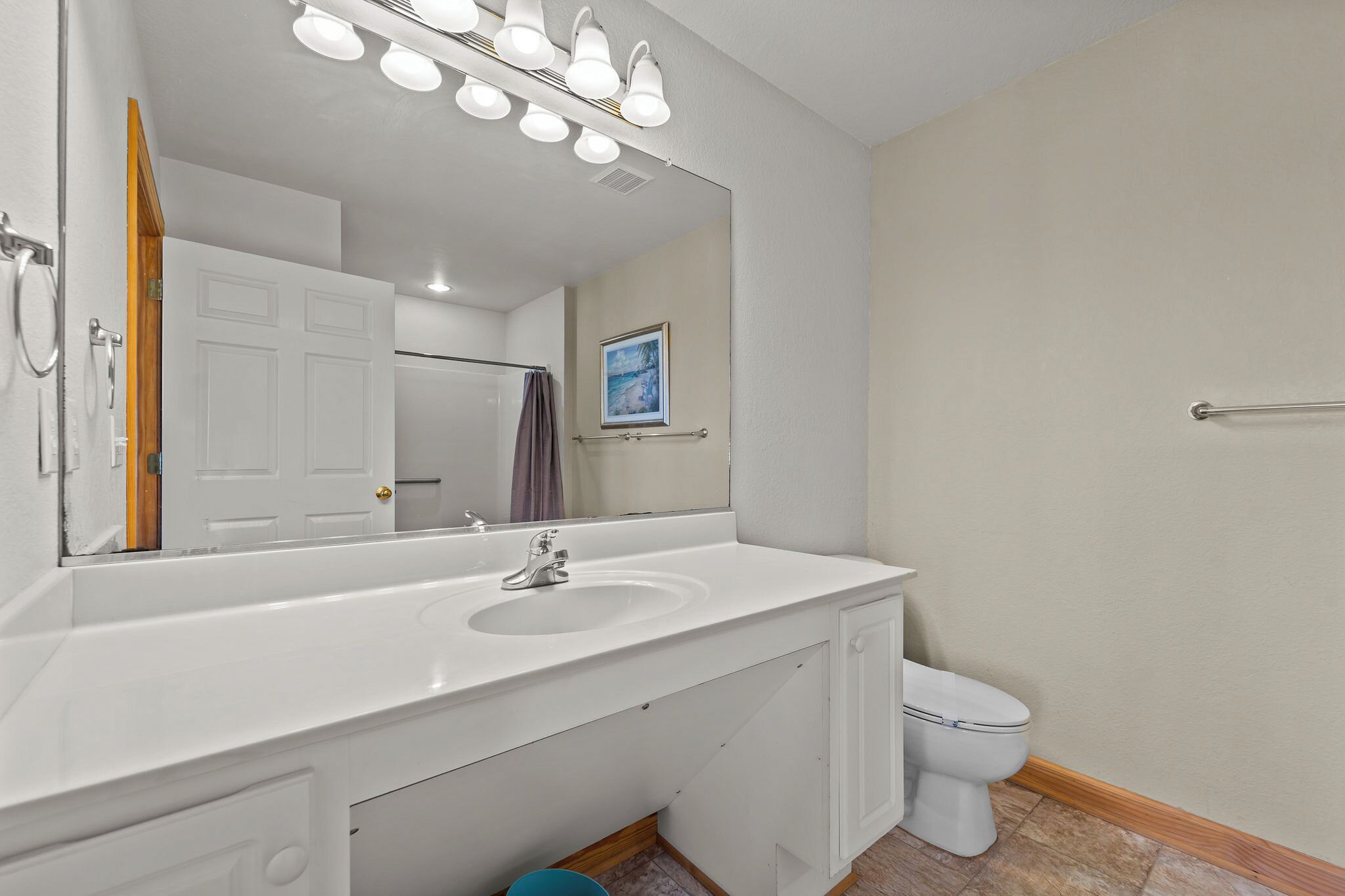 A bathroom with a white sink, mirror, and toilet. There is a shower curtain rod and a towel rack on the wall.