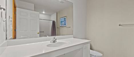 A bathroom with a white sink, mirror, and toilet. There is a shower curtain rod and a towel rack on the wall.