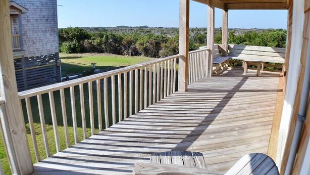 A wooden deck with a railing, benches, and a view of a building and landscape. - Awesome 'D' has a hot tub for your family vacation entertainment (South Nags Head)