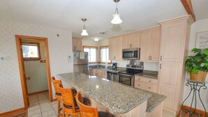 A kitchen with a granite countertop, wooden chairs, a refrigerator, a microwave, and a stove. - Awesome 'D' has a hot tub for your family vacation entertainment (South Nags Head)