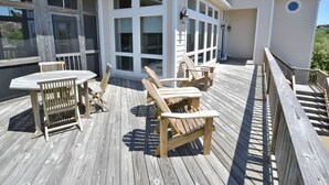 A wooden deck with a table and chairs, a covered area with large windows, and a white building with a balcony. - Once you arrive in Duck, North Carolina, you'll want to come and relax in Ducktron. (Duck)