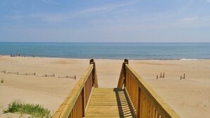 A wooden boardwalk leading to a sandy beach with the ocean in the background. - Fabulous oceanfront home, beautifully decorated with ocean to sound views. (South Nags Head)