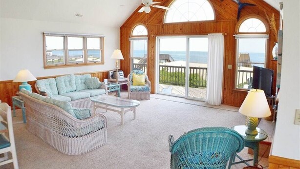 A spacious living room with a high ceiling, large windows, and a view of the ocean. - Fabulous oceanfront home, beautifully decorated with ocean to sound views. (South Nags Head)
