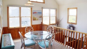 A dining area with a glass table and chairs, wooden walls, and large windows. - Fabulous oceanfront home, beautifully decorated with ocean to sound views. (South Nags Head)