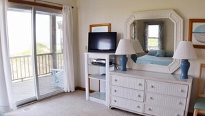 A hotel room with a large sliding glass door to a balcony, a flat-screen TV, a white dresser with two lamps, and a mirror above the dresser. - Fabulous oceanfront home, beautifully decorated with ocean to sound views. (South Nags Head)