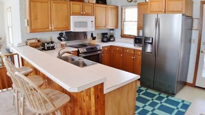A kitchen with wooden cabinets, a stainless steel refrigerator, a microwave, and a sink. - Fabulous oceanfront home, beautifully decorated with ocean to sound views. (South Nags Head)