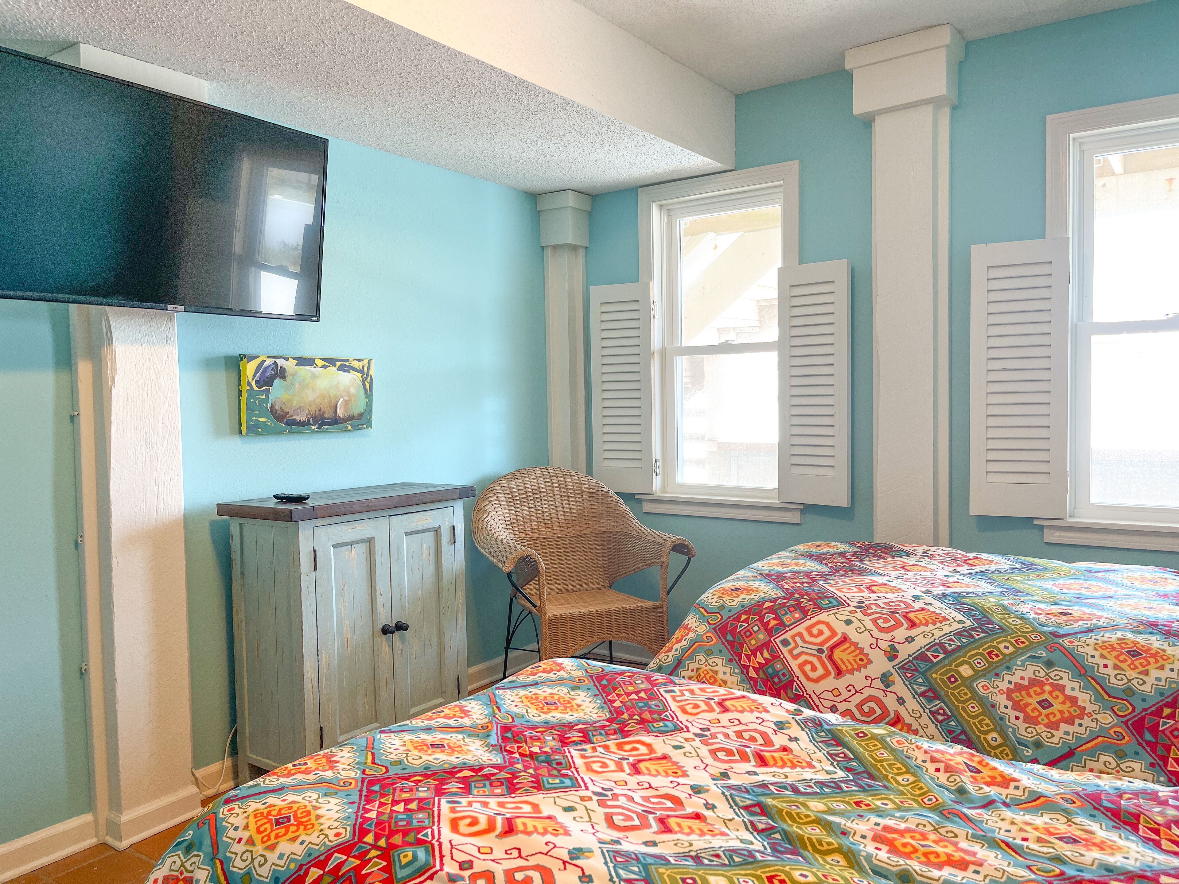 A bedroom with a bed, a television, a chair, and a window with shutters.