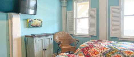 A bedroom with a bed, a television, a chair, and a window with shutters.