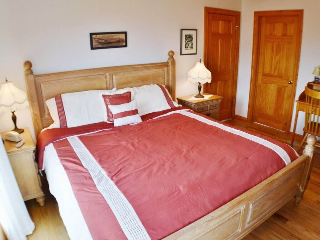 A neatly made bed with a red and white bedspread, wooden headboard, and two bedside tables with lamps.