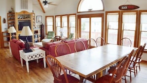 A spacious living room with a wooden dining table, red sofas, and a large window with a view. - When it is time to Set Back & Relax, you have found the vacation rental home to do just that. (Corolla)