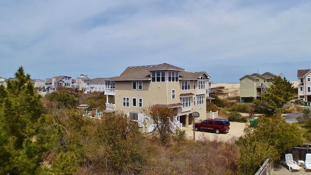 A coastal residential area with houses, a red car, and a clear sky. - When it is time to Set Back & Relax, you have found the vacation rental home to do just that. (Corolla)