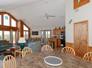 Relax in this spacious living area with a high ceiling and large windows, featuring a dining table, sofa, and kitchen area.
