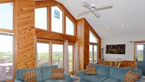 A spacious living room with two sofas, a ceiling fan, large windows, and a view of the outdoors. - Dreamcatcher is a well-equipped vacation home perfect for a terrific vacation experience. (Corolla)