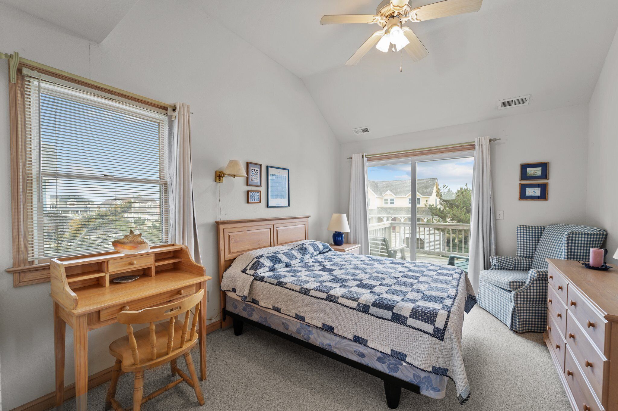 A bedroom with a bed, a desk, a chair, a dresser, and a ceiling fan.