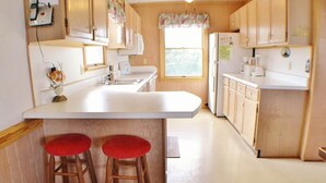 Cocina con armarios de madera, encimera blanca y dos taburetes rojos.