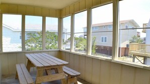 A covered patio with a wooden table and benches, large windows offering views of the neighborhood. - Just across the street from the beach, “Pope” is perfect for a small family. (South Nags Head)