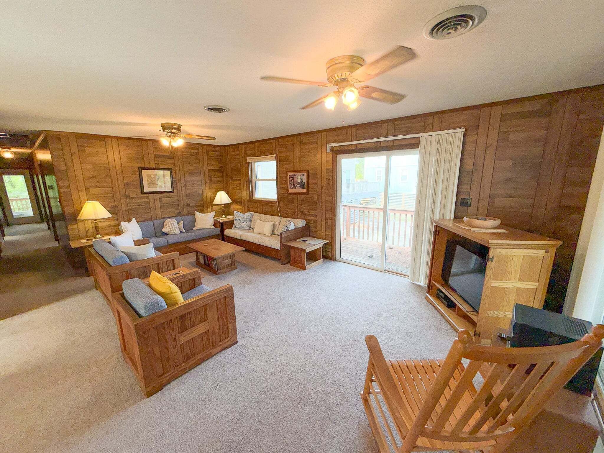 A cozy living room with wooden walls, a sofa set, a coffee table, a TV, and a fireplace.