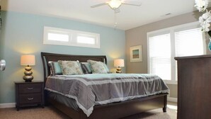 A bedroom with a bed, two bedside tables with lamps, a ceiling fan, and a window with blinds. - Charming Outer Banks Home (Kill Devil Hills)