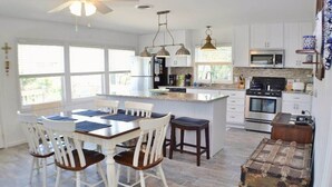Une cuisine moderne avec des meubles blancs, un îlot central et un coin repas avec des chaises blanches.
