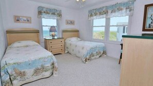 Un dormitorio con dos camas, un ventilador de techo, una mesita de noche y una ventana con vista al mar.