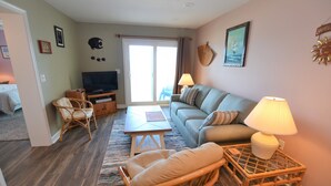 Un salon avec un canapé, deux fauteuils, un téléviseur et une lampe.