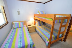 A bedroom with two single beds, a bunk bed, a nightstand with a lamp, and a small wall decoration. - Book into Brooks and you will not be disappointed! (Nags Head)