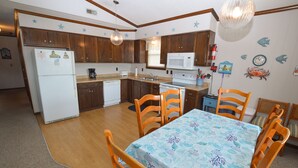 Una cocina compacta con armarios de madera, un refrigerador blanco, un microondas y una zona de comedor con mesa y sillas.