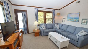 Una sala de estar con un sofá modular, un televisor sobre un mueble de madera, una mesa de centro blanca y una lámpara.
