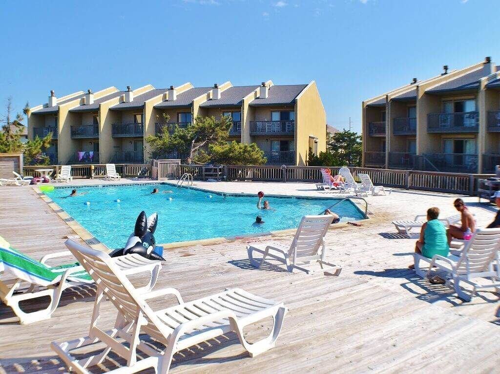 A pool area with lounge chairs and a wooden deck, surrounded by multi-story buildings with balconies.