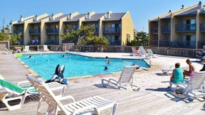 A pool area with lounge chairs and a wooden deck, surrounded by multi-story buildings with balconies.