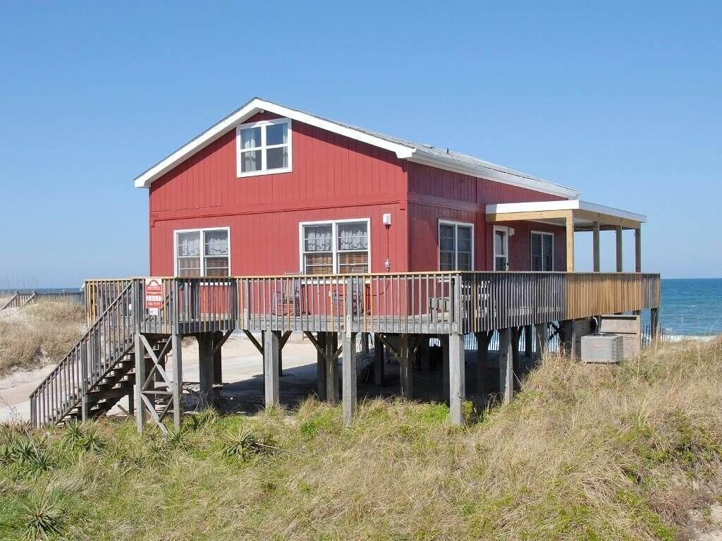 Ein rotes Gebäude mit einer Holzterrasse und einer Treppe zum Strand.
