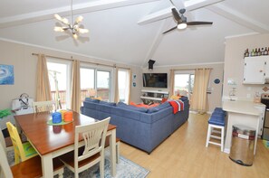 Un grand espace de vie comprenant un canapé, une table à manger, des chaises, un téléviseur et un ventilateur de plafond.