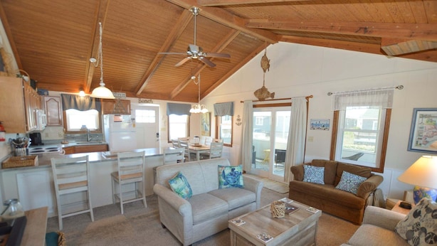 A spacious living area with a kitchen, a dining table, and two sofas. - Listen to the waves break and look for dolphins right from your screened-in porch! (South Nags Head)