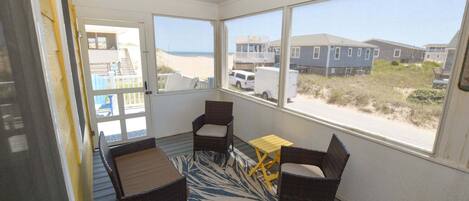 A room with a view of the beach, wicker furniture, and a small table.