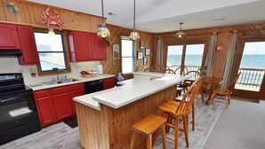 A kitchen with a central island, red cabinets, and a view of the ocean. - This charming beach house is the perfect year-round retreat. (South Nags Head)