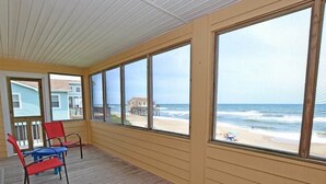 A covered porch with large windows overlooking a beach. - This charming beach house is the perfect year-round retreat. (South Nags Head)