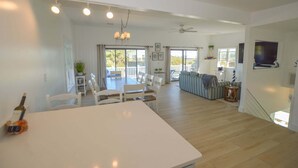 A spacious living area with a dining table, chairs, a sofa, and a television mounted on the wall.