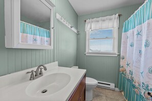 A bathroom with a white sink, a mirror, a towel rack, a toilet, and a window with blinds.