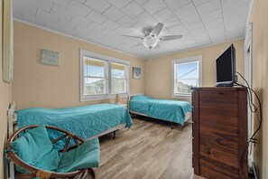 A room with two beds, a ceiling fan, a TV on a wooden cabinet, and a window with blinds.