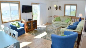 A spacious living room with a large window, a flat-screen TV, a sofa, a chair, and a coffee table.