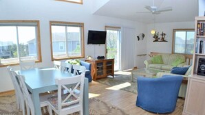 A spacious living room with a dining area, large windows, and a flat-screen TV.