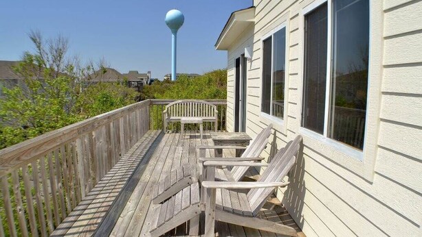 A wooden deck with a table and chairs, a railing, and a building with large windows.