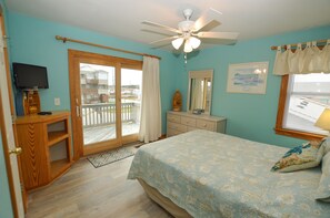 Relax in this serene bedroom with a large bed, ceiling fan, and TV, surrounded by a dresser and mirror.