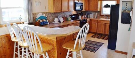Una cocina con armarios de madera, una isla central con taburetes de bar, un microondas y un refrigerador.