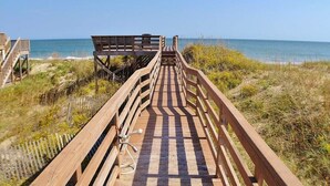 Une promenade en bois qui mène à une plage d’où l’on a une vue dégagée sur l’océan.