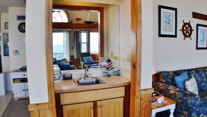 Une cuisine compacte avec des meubles en bois, un évier et un petit plan de travail. On y trouve également un coin repas avec un canapé à motifs et une petite table.